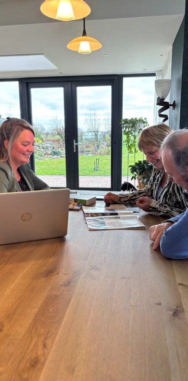 Reis op maat samenstellen samen met de klant Drie mensen aan een houten tafel, met een laptop en documenten, in een lichte ruimte.
