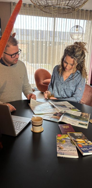 Een reis op maat samen stellen Een man en vrouw bladeren door tijdschriften aan een tafel met een laptop.
